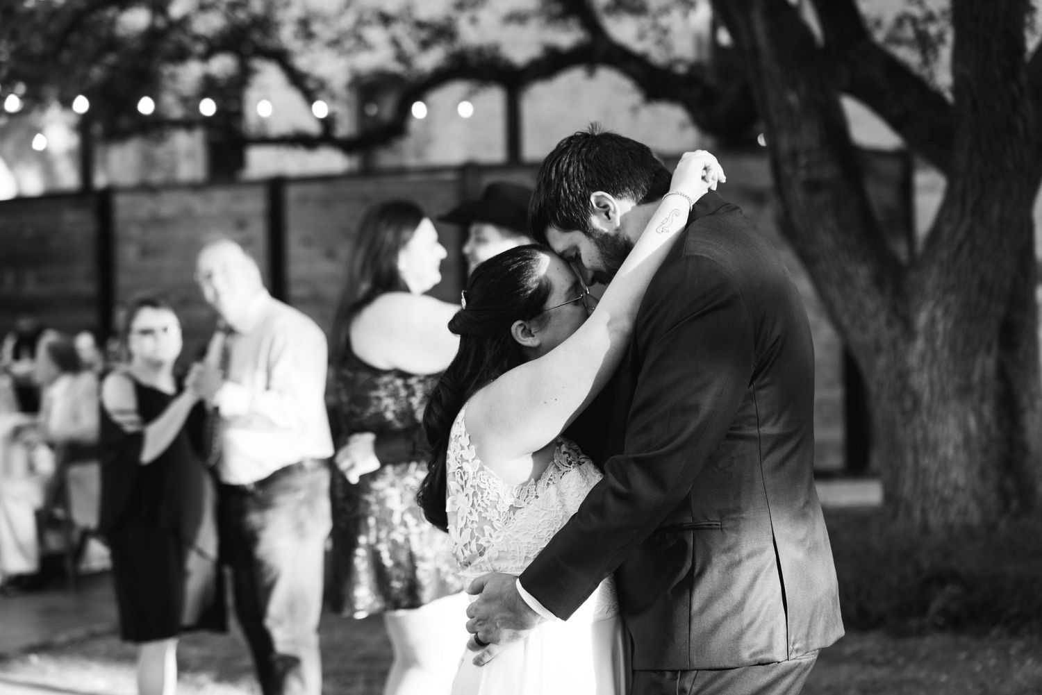 A black and white photo captures a romantic dance moment at an outdoor wedding reception.