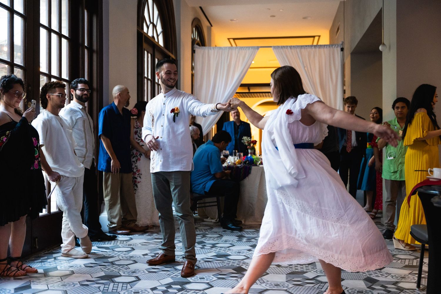 Dancers twirl and move on an ornate tiled floor while guests watch during a celebration event.