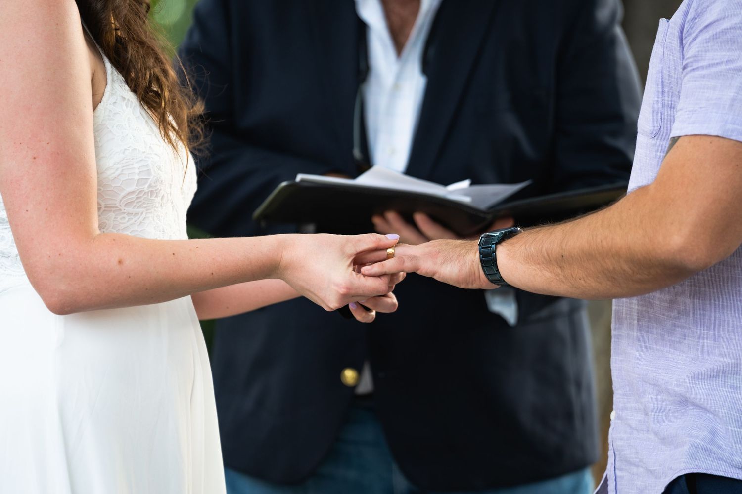 Close up of hands exchanging rings during an outdoor wedding ceremony.