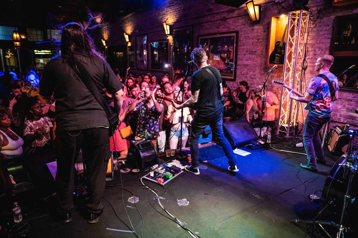 Wide shot of band performing for energetic crowd in a dimly lit music venue.