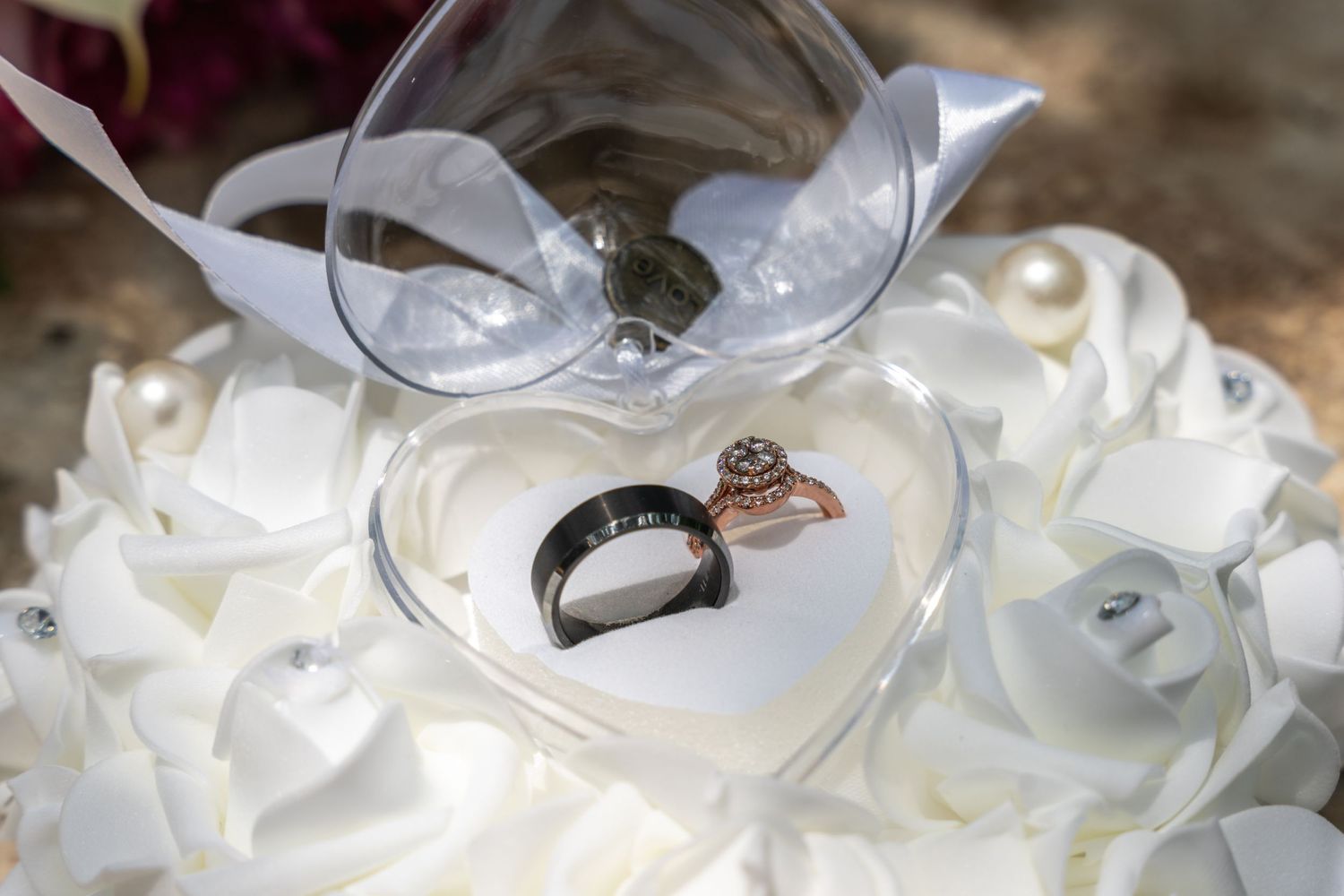 Wedding rings displayed in heart-shaped container surrounded by white roses.