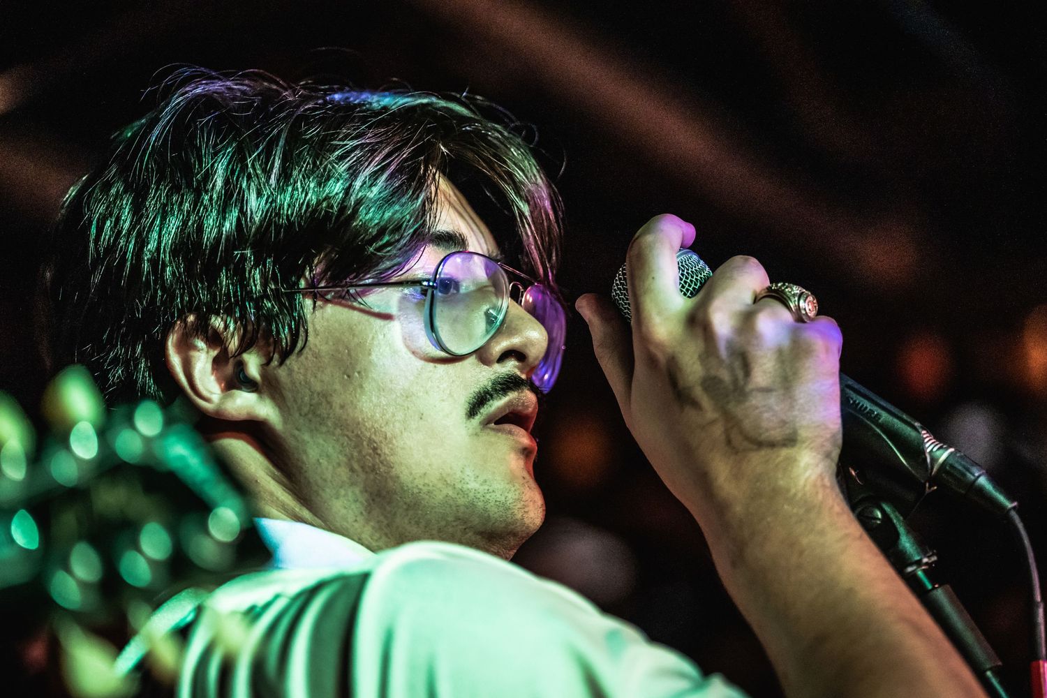Singer with glasses performs passionately under green stage lighting.