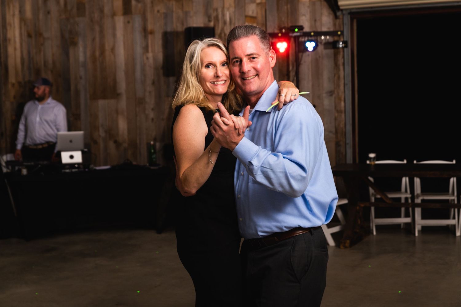 A couple shares an intimate slow dance moment in a rustic barn setting.