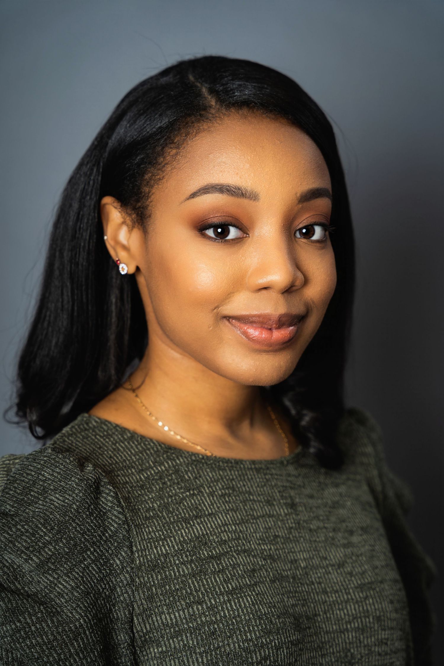 Close-up portrait showing radiant smile and natural makeup against soft grey studio background.
