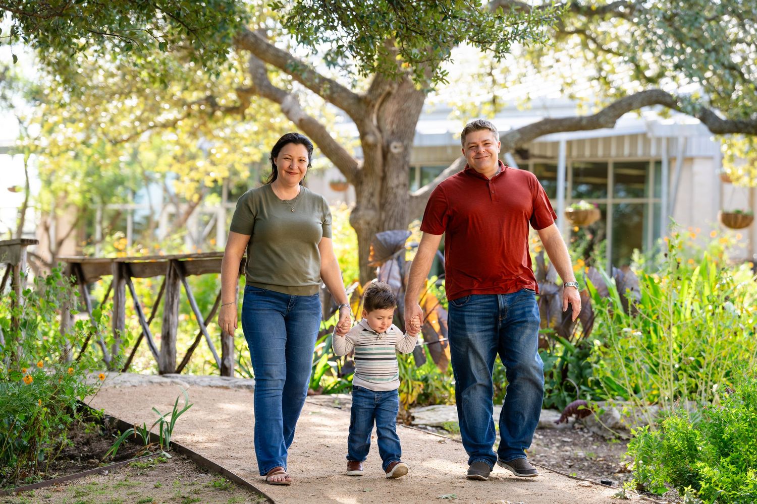 Family walking and holding hands together on a tree-lined path in a park during golden hour sunlight.