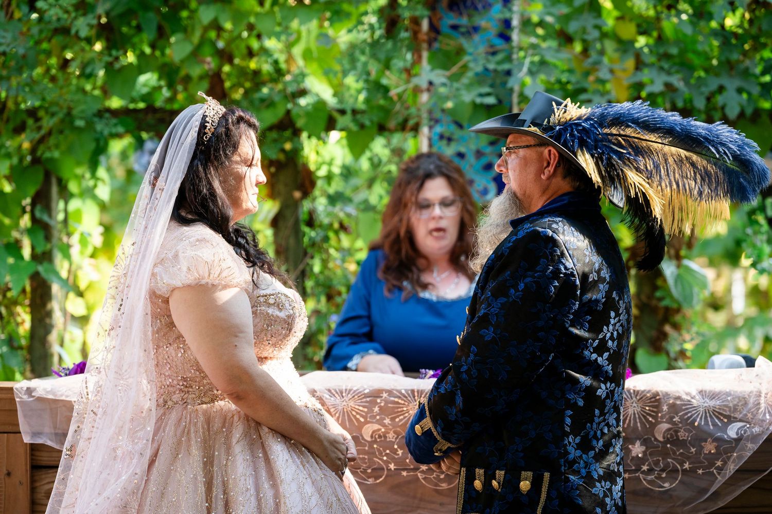 A couple shares a romantic moment during an outdoor wedding ceremony under green trees and natural lighting.