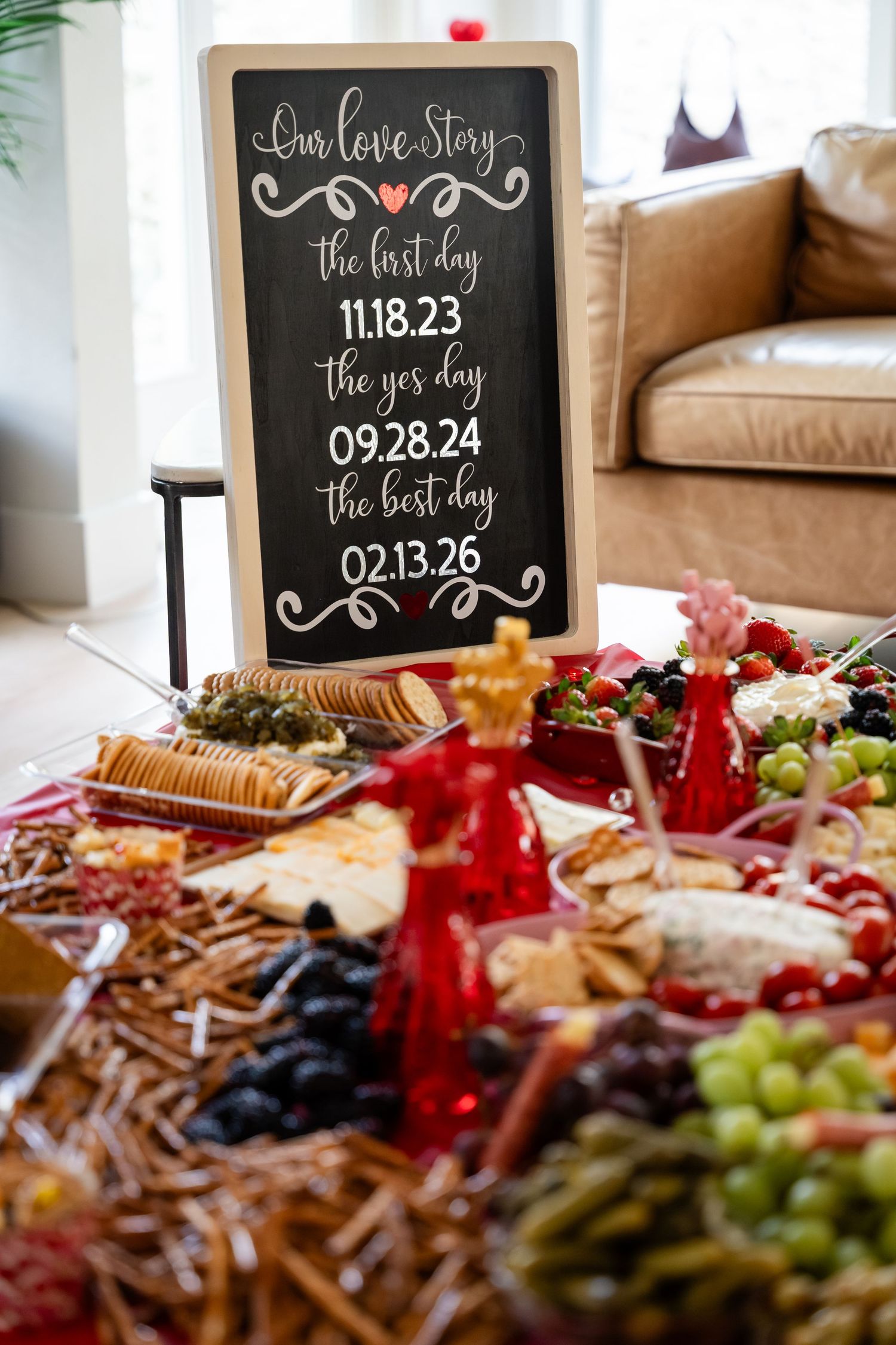Chalkboard love story sign with key dates displayed beside an elegant charcuterie board with fruits and crackers.