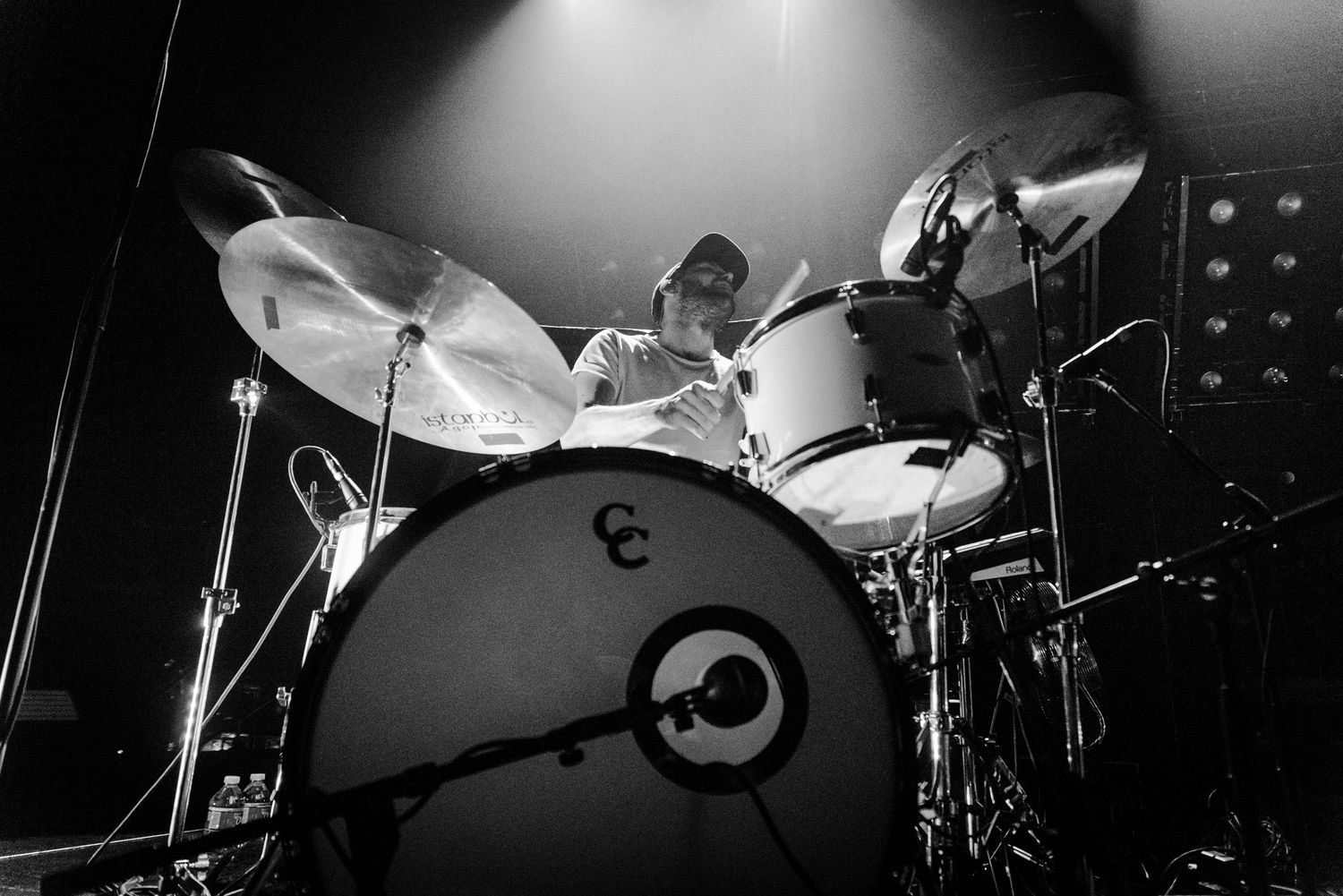 A black and white photo of a drum kit on stage with dramatic lighting and cymbals in focus.
