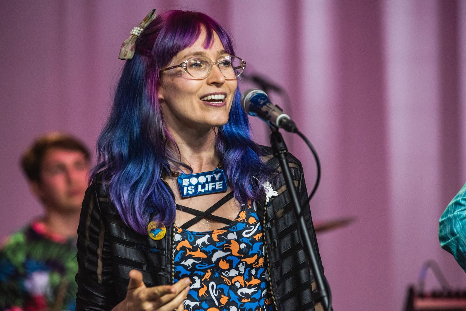 Singer performs on stage wearing a blue and orange patterned dress with glasses and colorful hair.