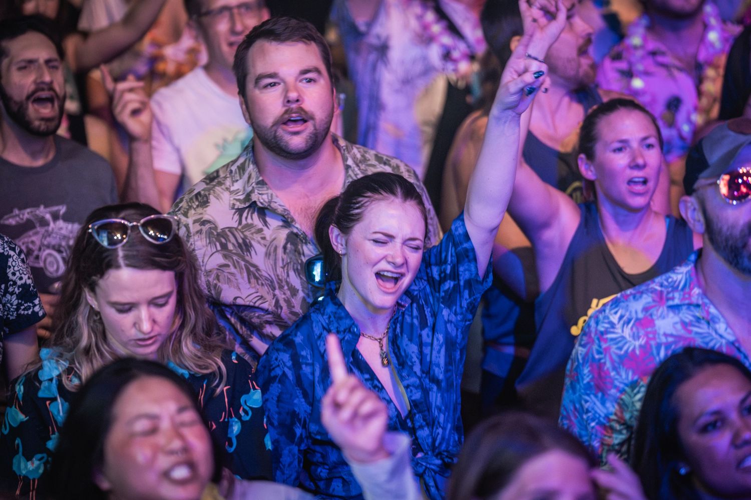 Concert crowd enjoying live music with colorful purple and blue lighting effects in a packed venue.