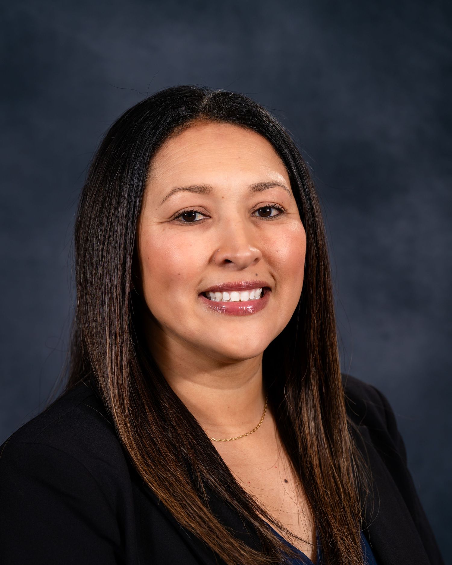 Professional headshot portrait against dark background showing warm smile and long dark hair.