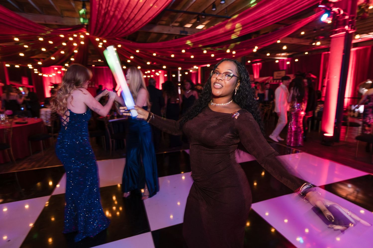 People dancing in a dark venue with pink lighting and glowing decorations illuminating the dance floor.
