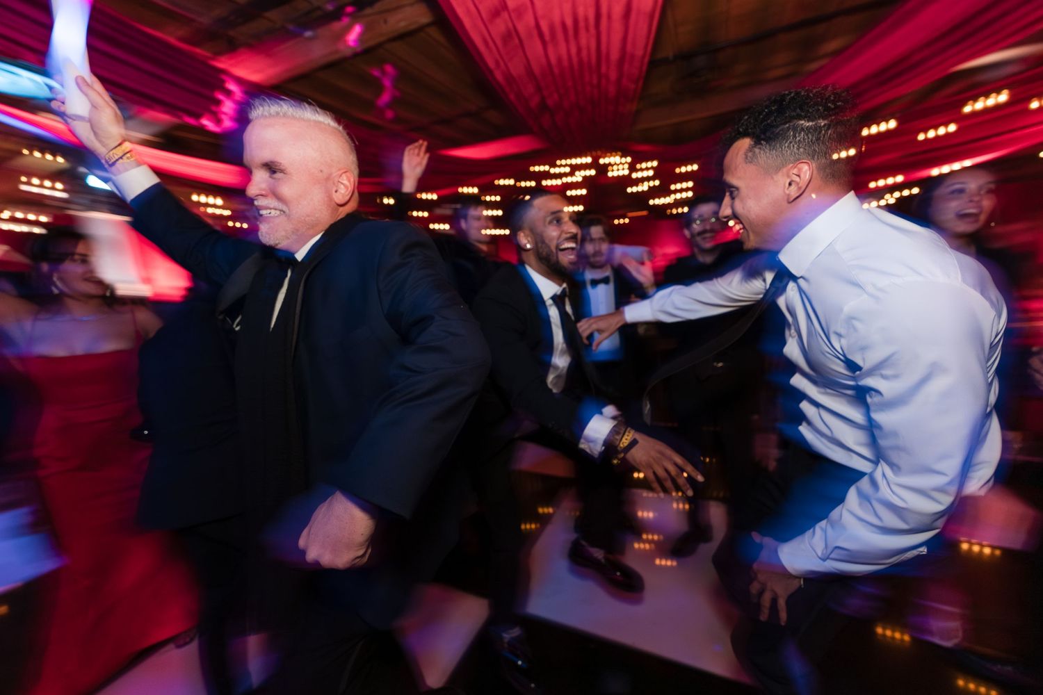 People dancing and celebrating at a lively party with red lighting and a festive atmosphere.