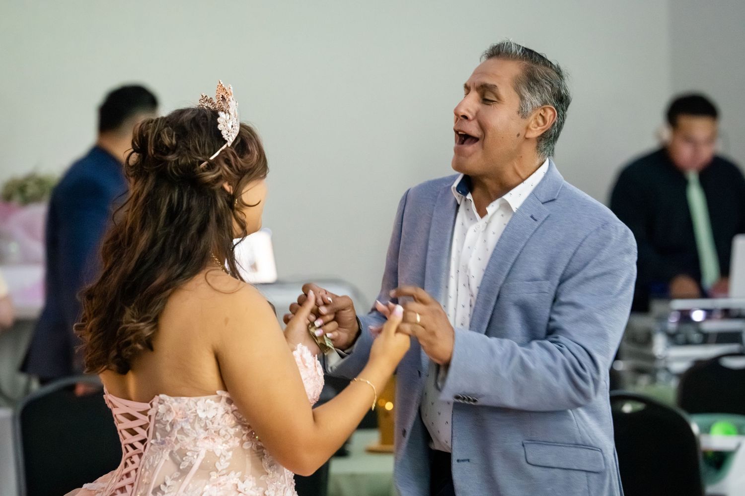A man in a blue suit dances with a young woman in a pink gown at a quinceañera celebration.