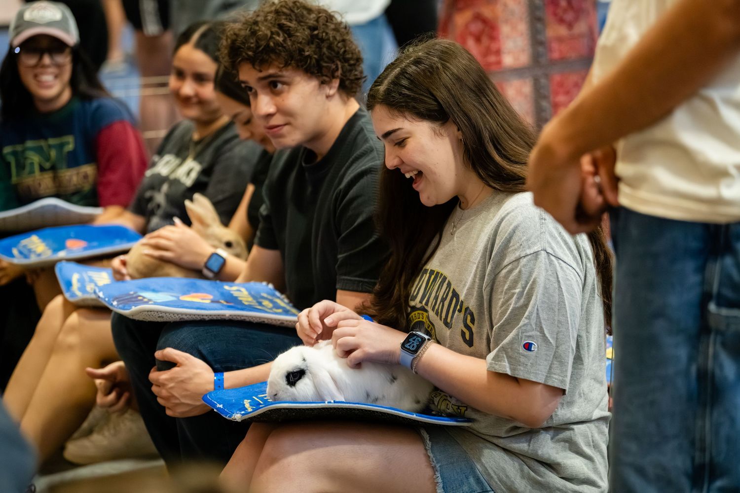 Students smile and pet a white dog during a college orientation event, holding informational folders.