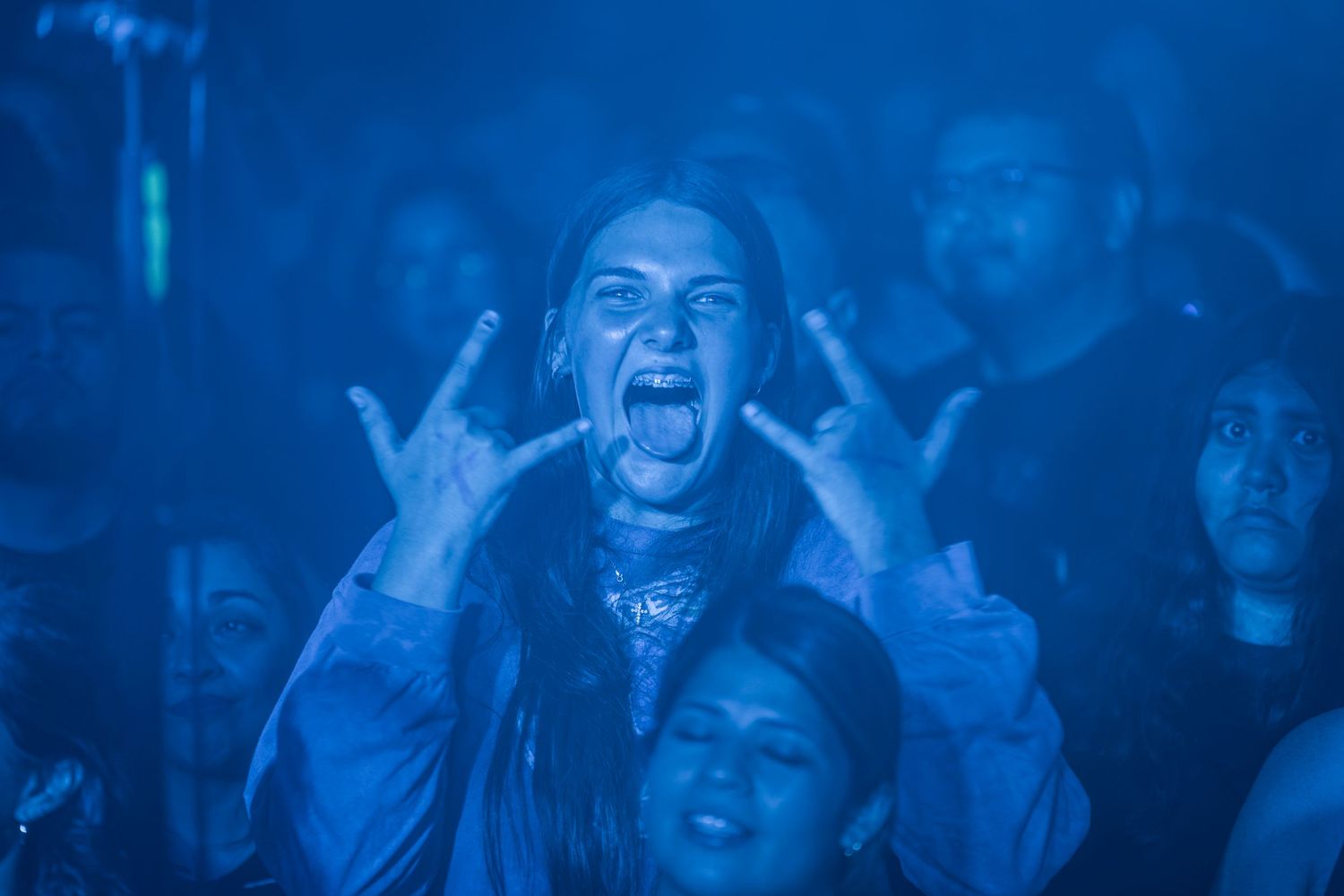Concert crowd cheers and celebrates with hands raised during a high-energy live music performance in blue lighting.