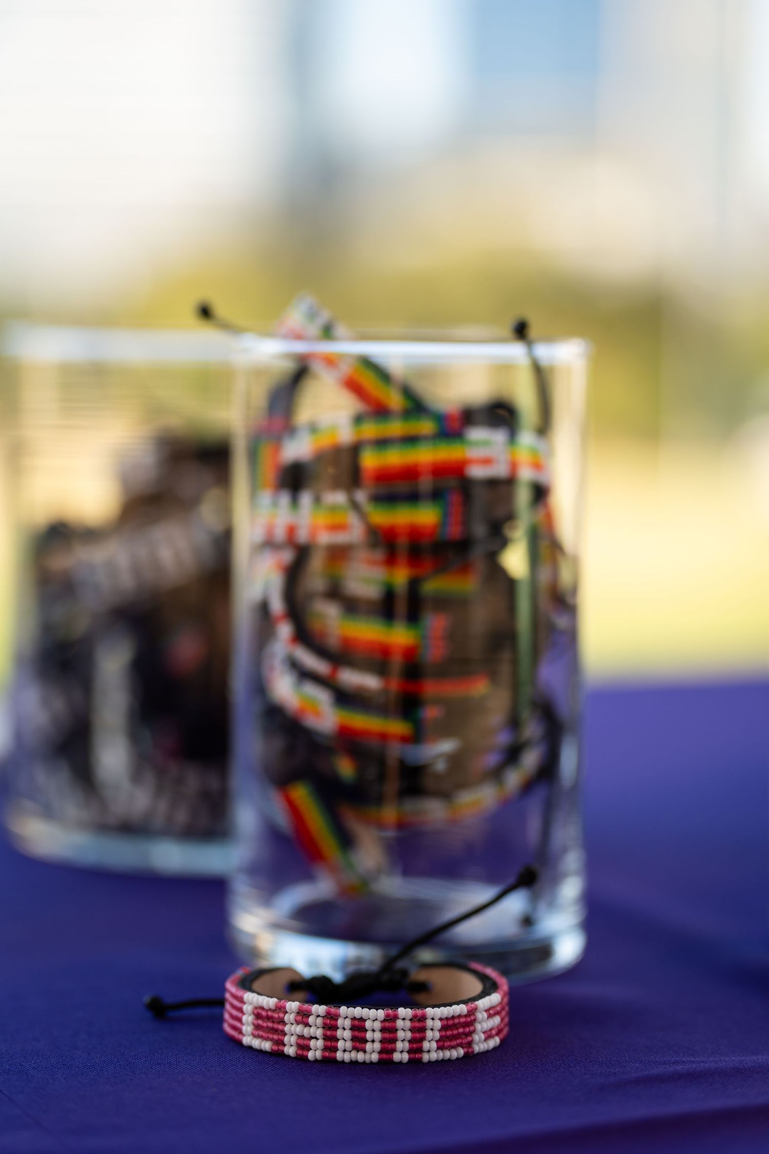 Colorful friendship bracelets displayed in clear glass containers on purple tablecloth.