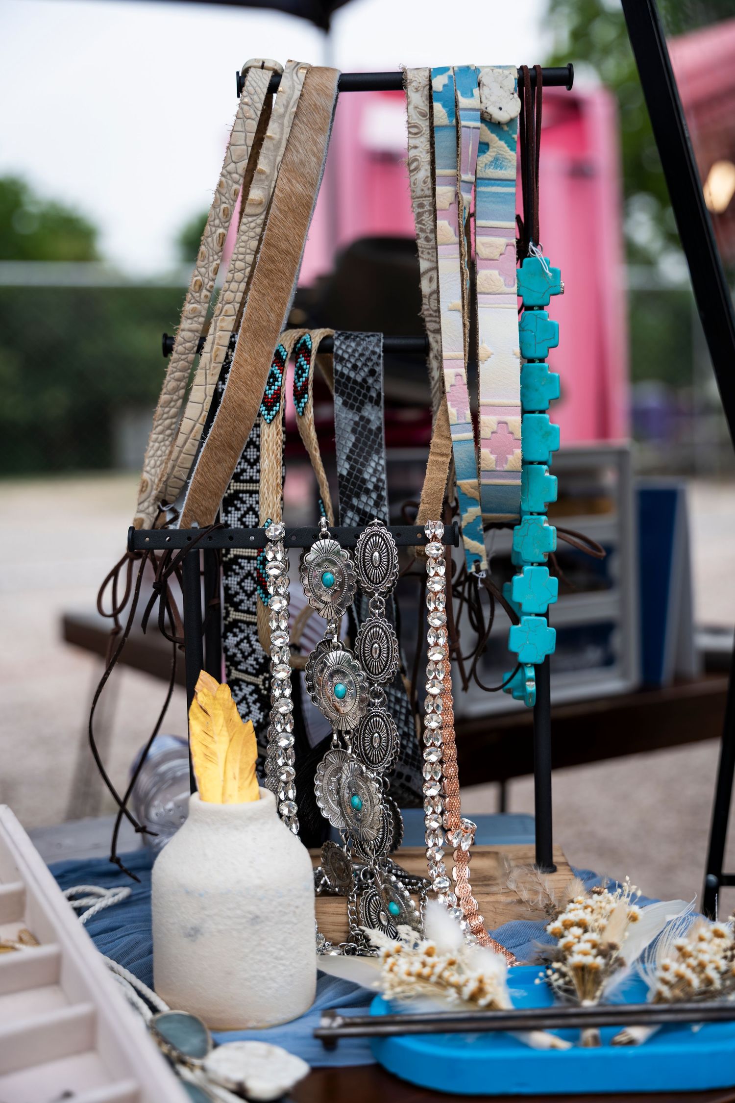 Rustic table display with turquoise and brown necklaces hanging from distressed wooden stands on blue fabric.