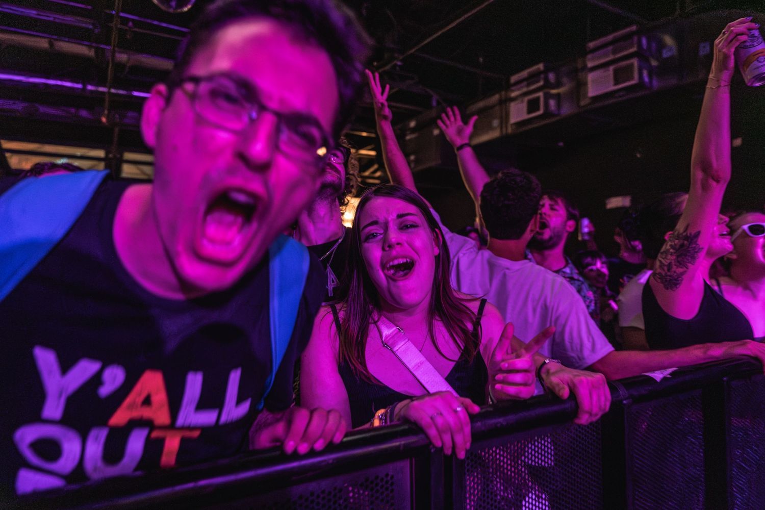 Concert attendees cheer and sing along at barrier during live music performance.