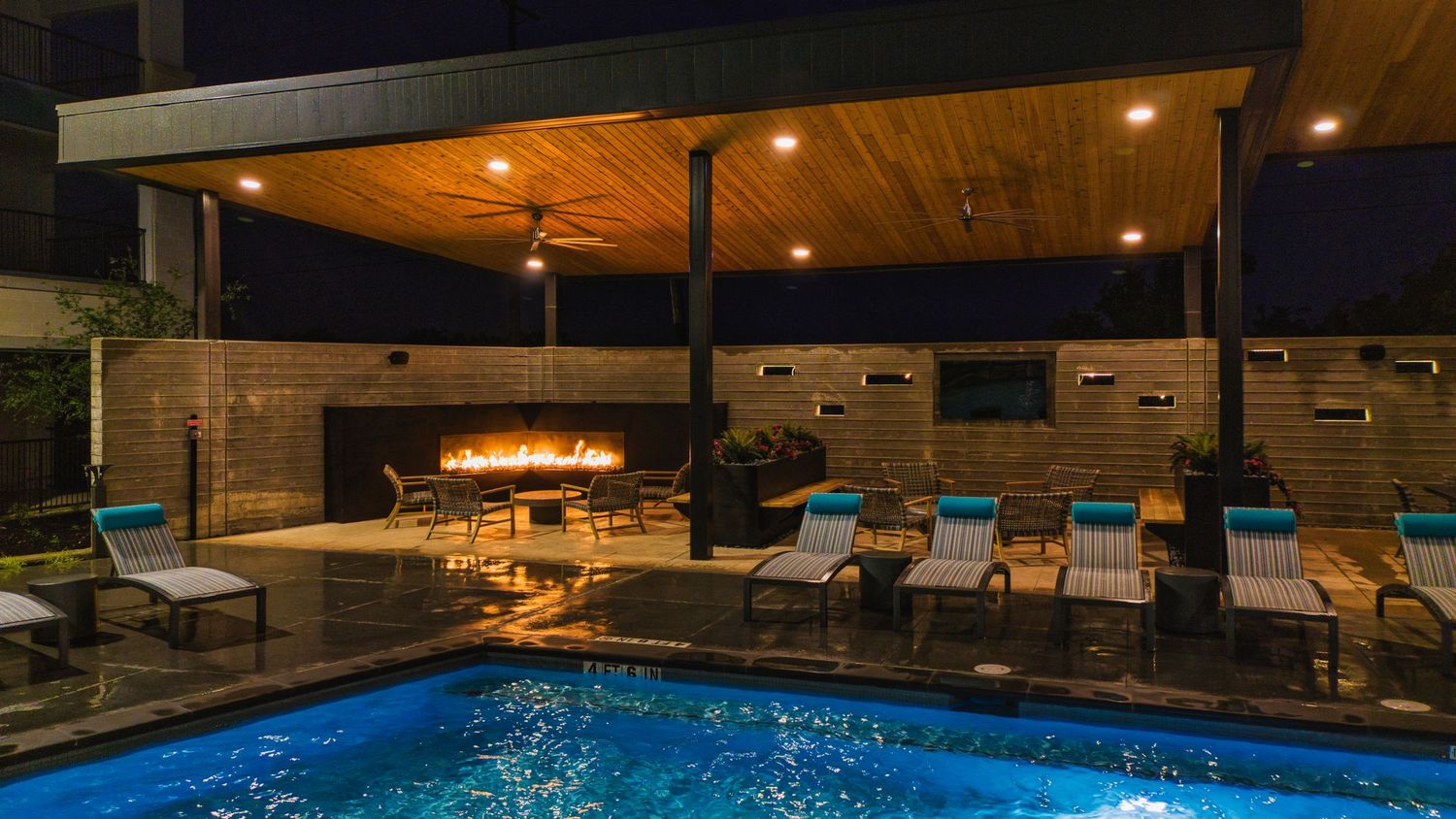 Cozy pool area featuring a fire pit lounge space and comfortable deck chairs under wooden pergola.