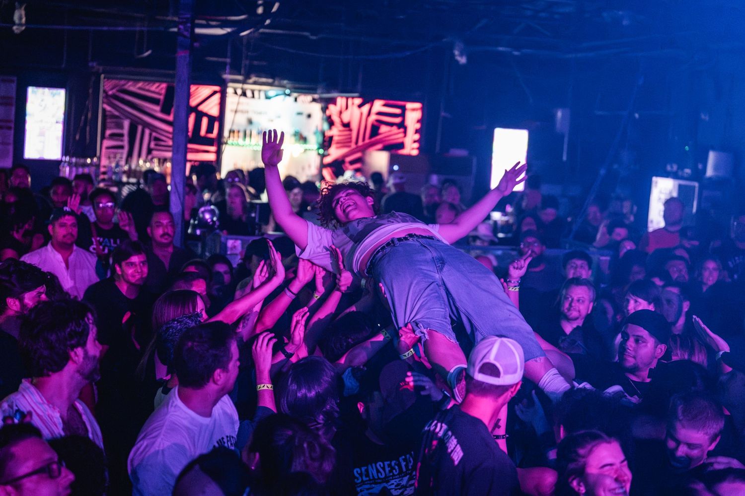 Energetic concert crowd surfing scene illuminated by purple stage lights.