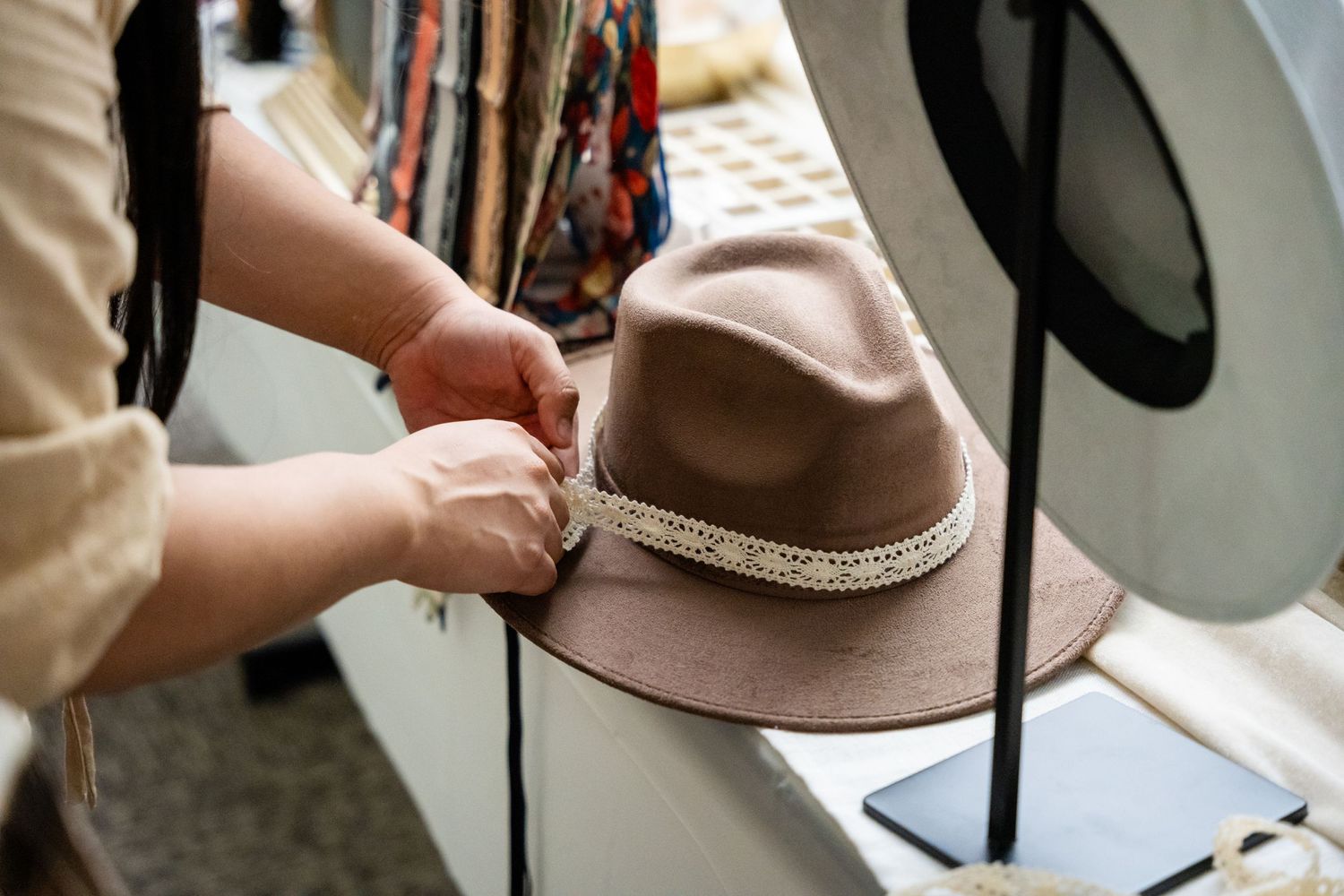 Close-up of hands adjusting a decorative trim on a brown fedora hat.