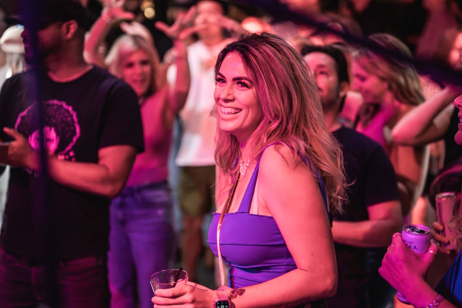 A concert-goer enjoys the show in a purple-lit venue with a crowd visible behind her.