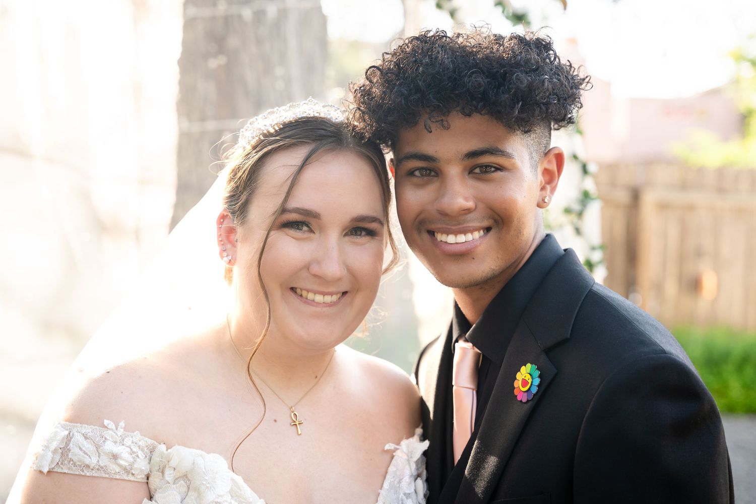Newlywed couple shares intimate portrait outdoors with groom wearing decorative boutonniere pin.