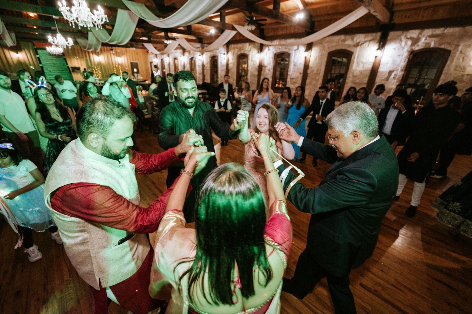 Dancing guests celebrating under green party lights in a rustic wooden venue.