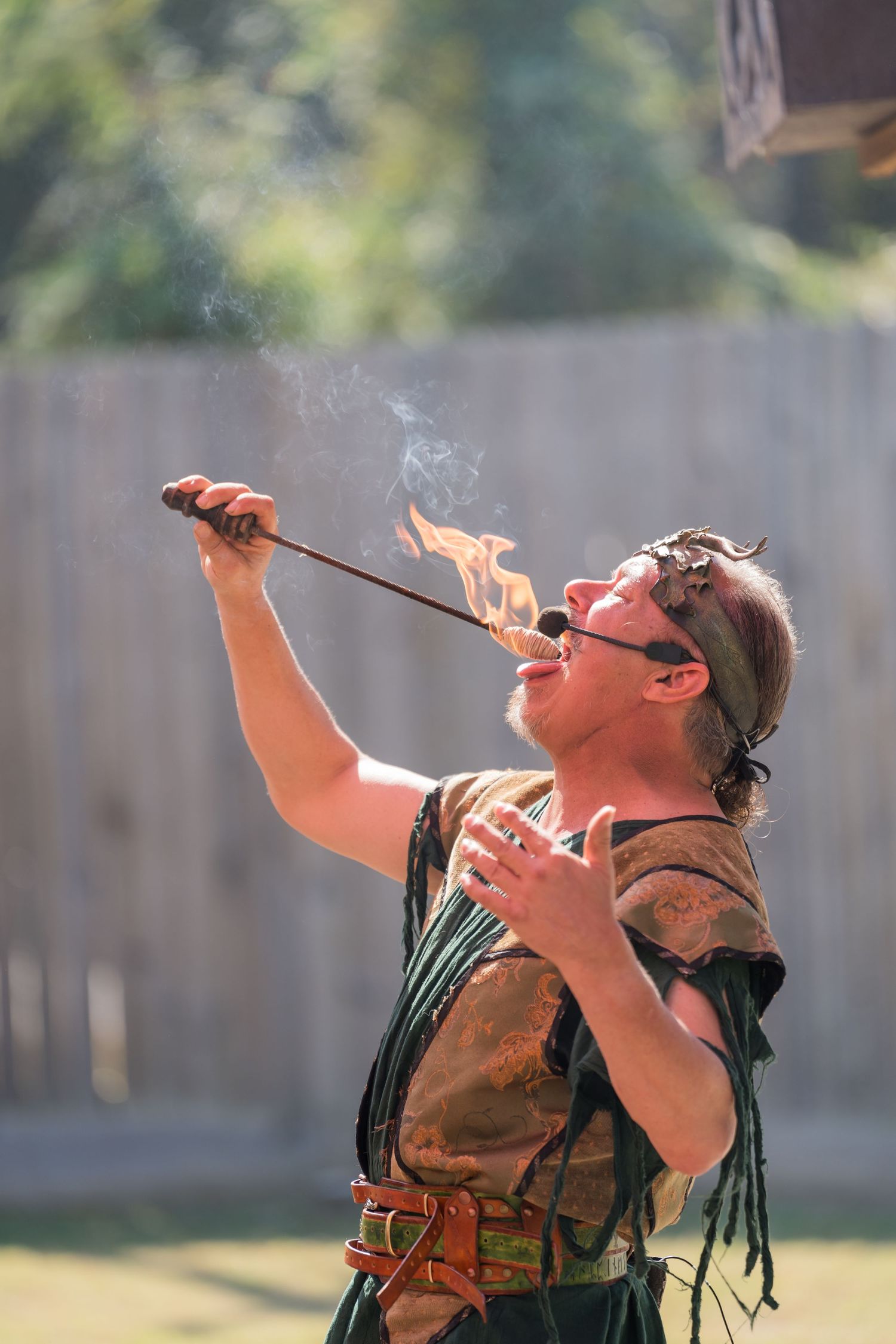 A performer breathes fire during an outdoor renaissance festival demonstration.