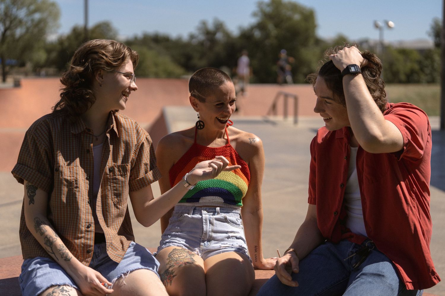 Three friends relaxing and socializing at a skate park on a sunny day.