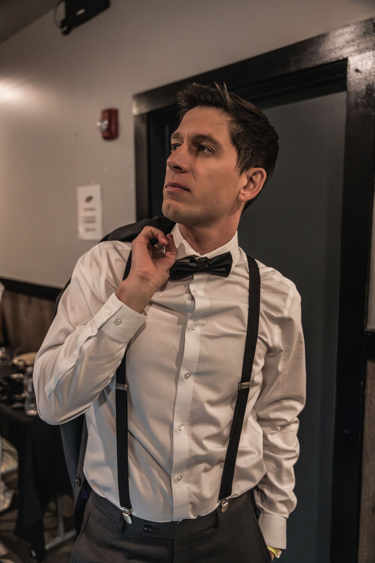 A performer adjusts his bowtie while getting ready in a dressing room.