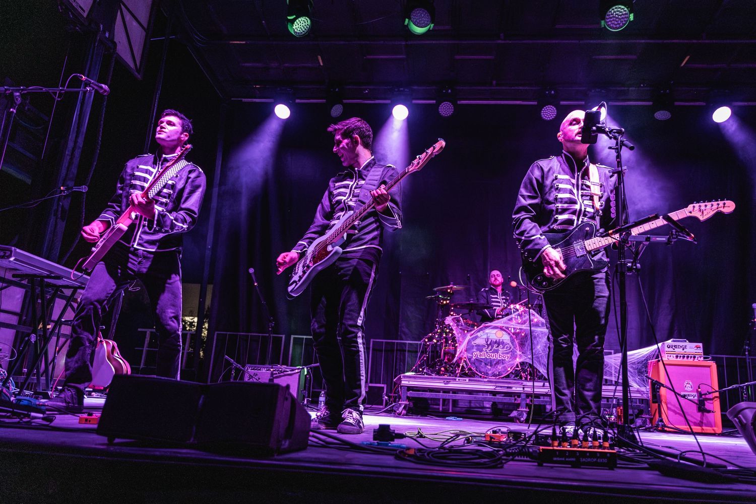 Band performs on stage with purple lighting and musical instruments during a live concert.