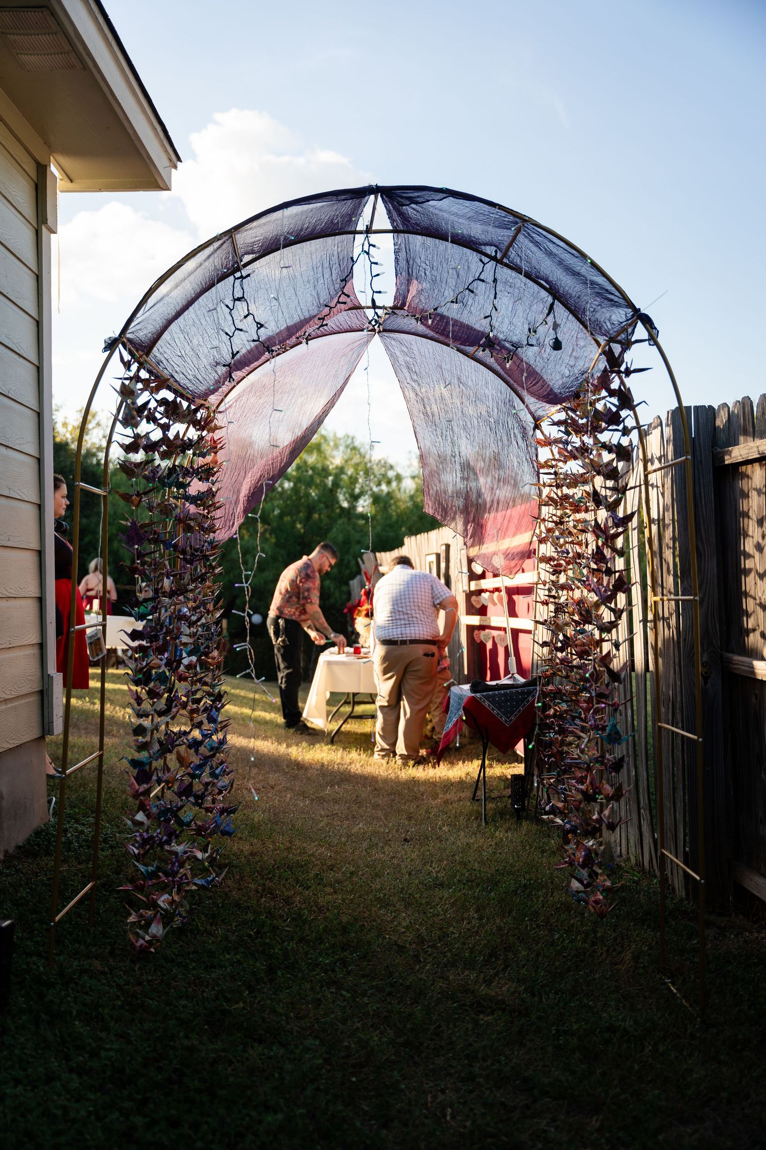 A decorated wedding arch with hanging ornaments and lights at an outdoor ceremony.