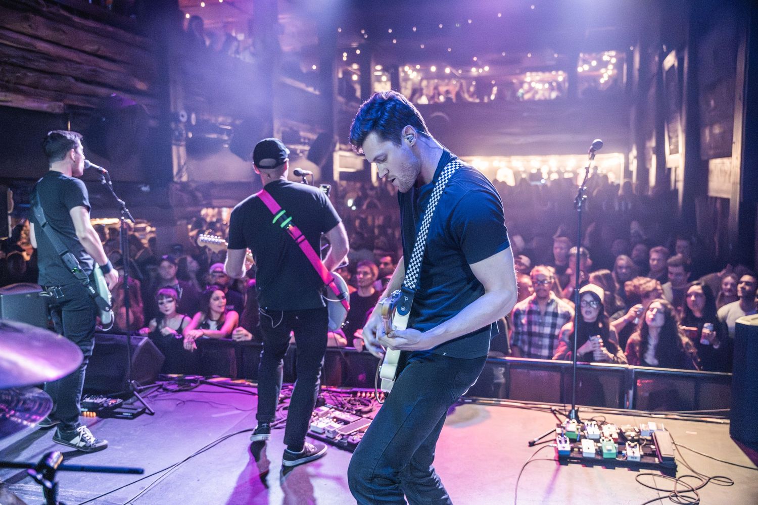 Band performing on stage with crowd visible in background under blue lighting.
