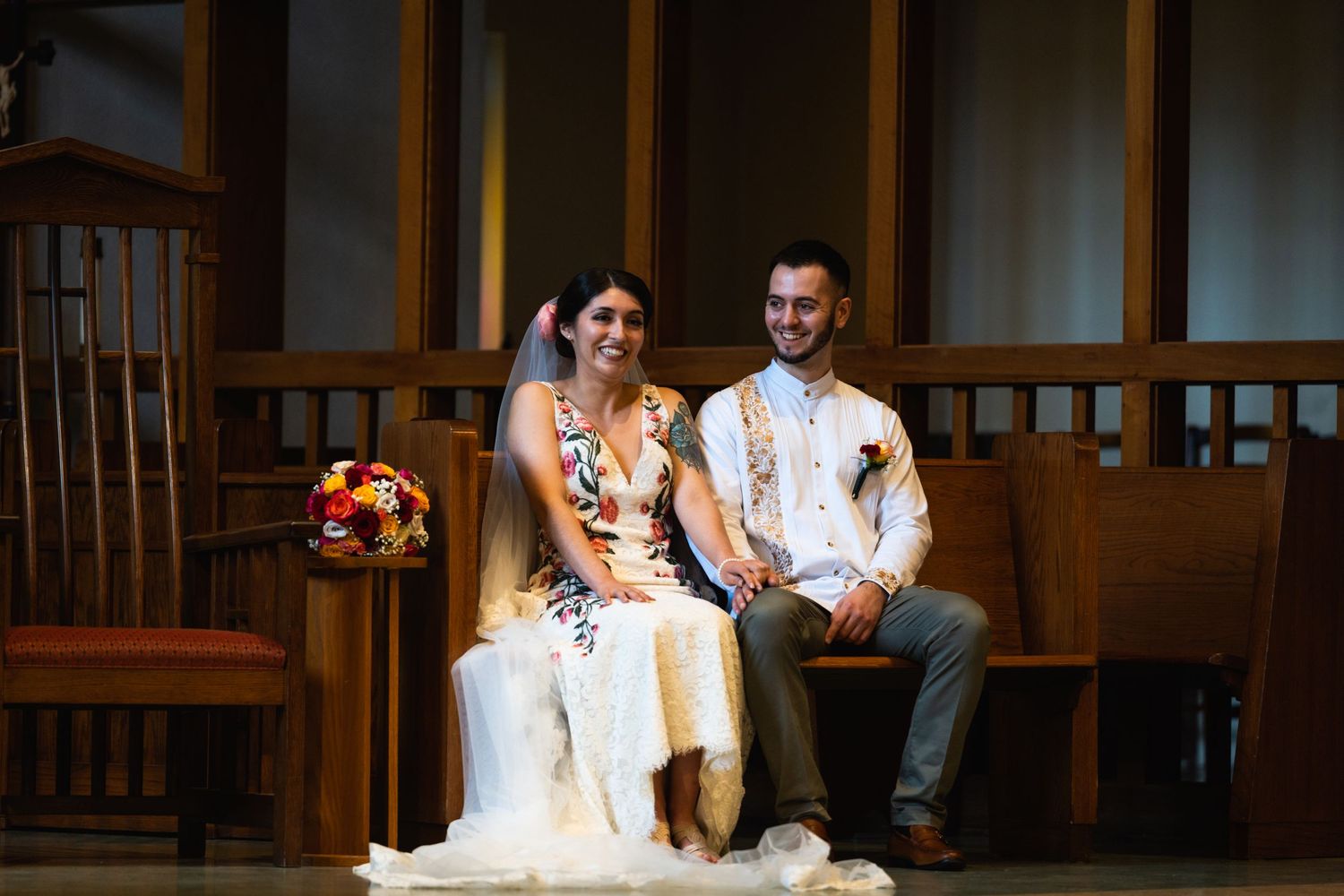 Couple sits together on wooden bench during their indoor wedding ceremony.