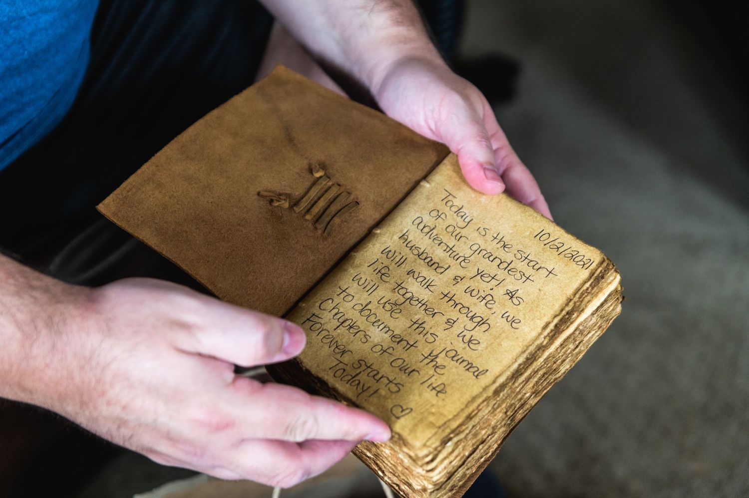Hands holding an aged brown leather book with handwritten text on yellowed pages.