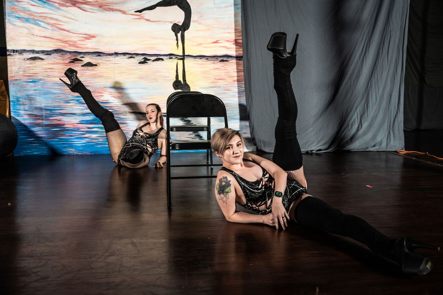 Dancers perform an artistic routine on a studio floor with a sunset backdrop and dramatic lighting.