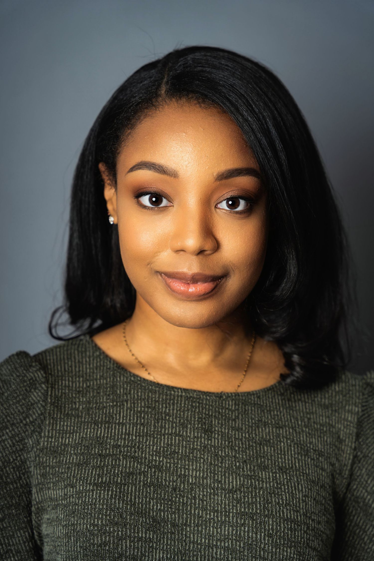Elegant headshot featuring a woman in a dark sweater with glossy black hair against grey background.