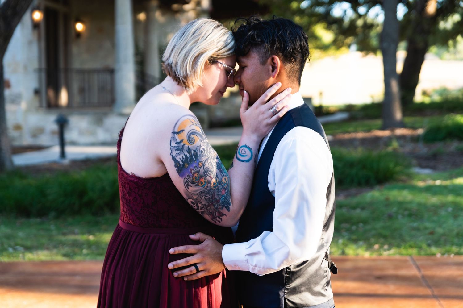 Two people share an intimate moment during a wedding celebration in an outdoor garden setting.