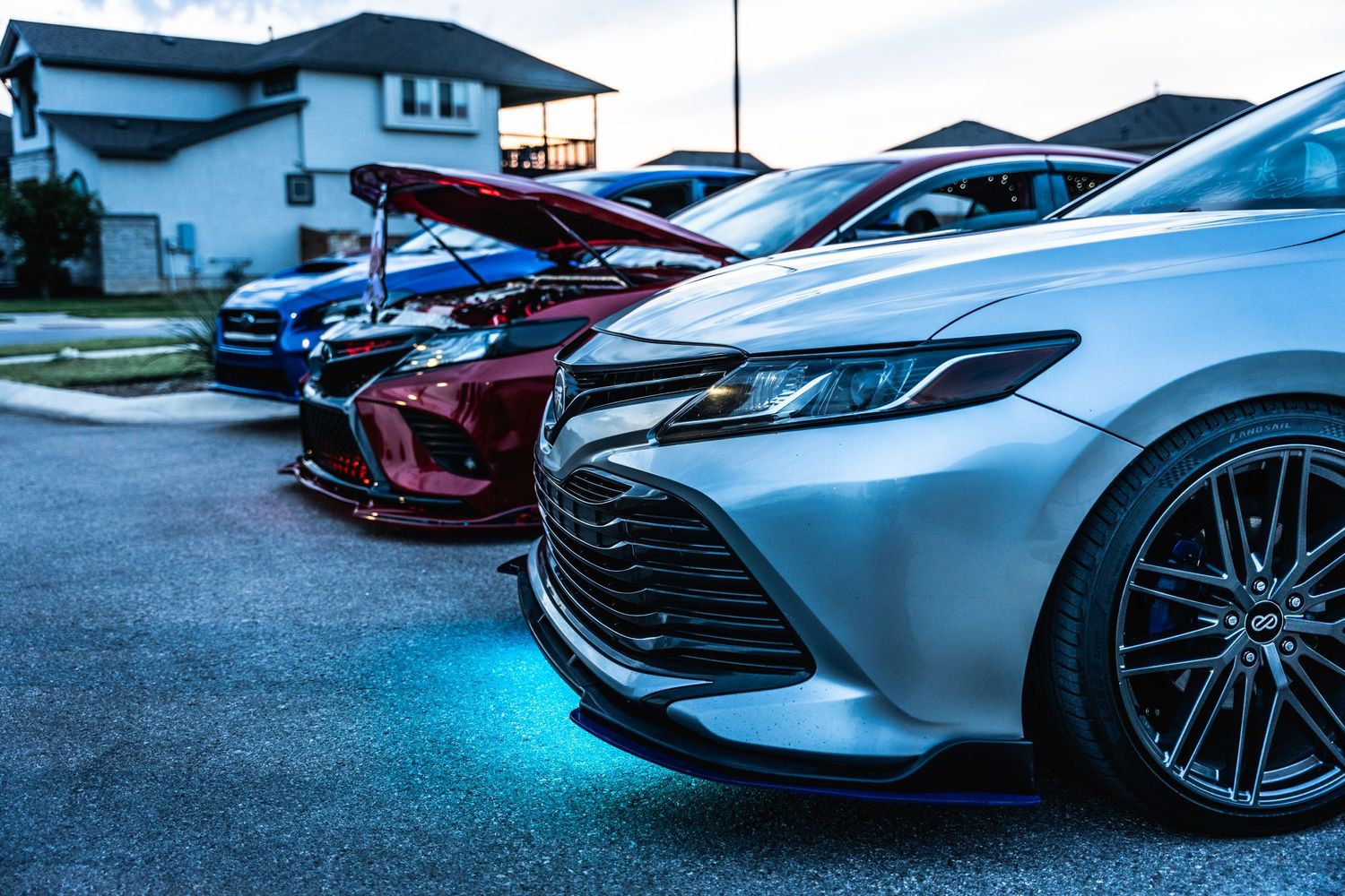 Row of modified cars featuring custom Toyota Camry with blue underglow lighting at night.