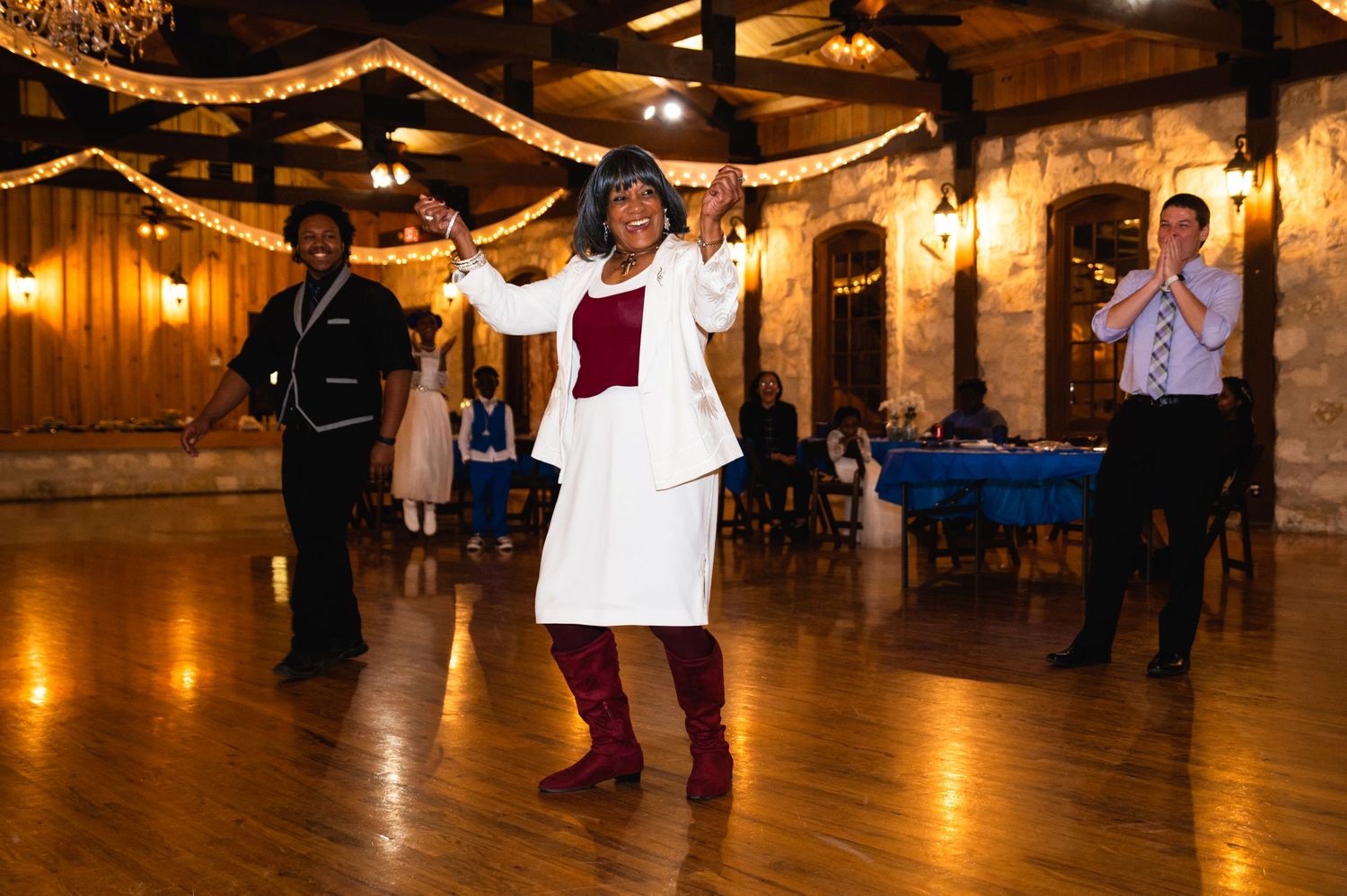 A celebratory dance moment captured in a rustic venue decorated with twinkling lights and wooden walls.