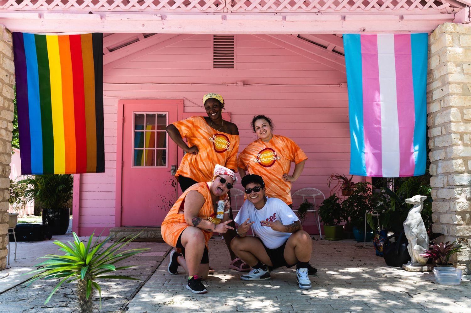 A group in orange shirts poses in front of a pink building with pride flags.