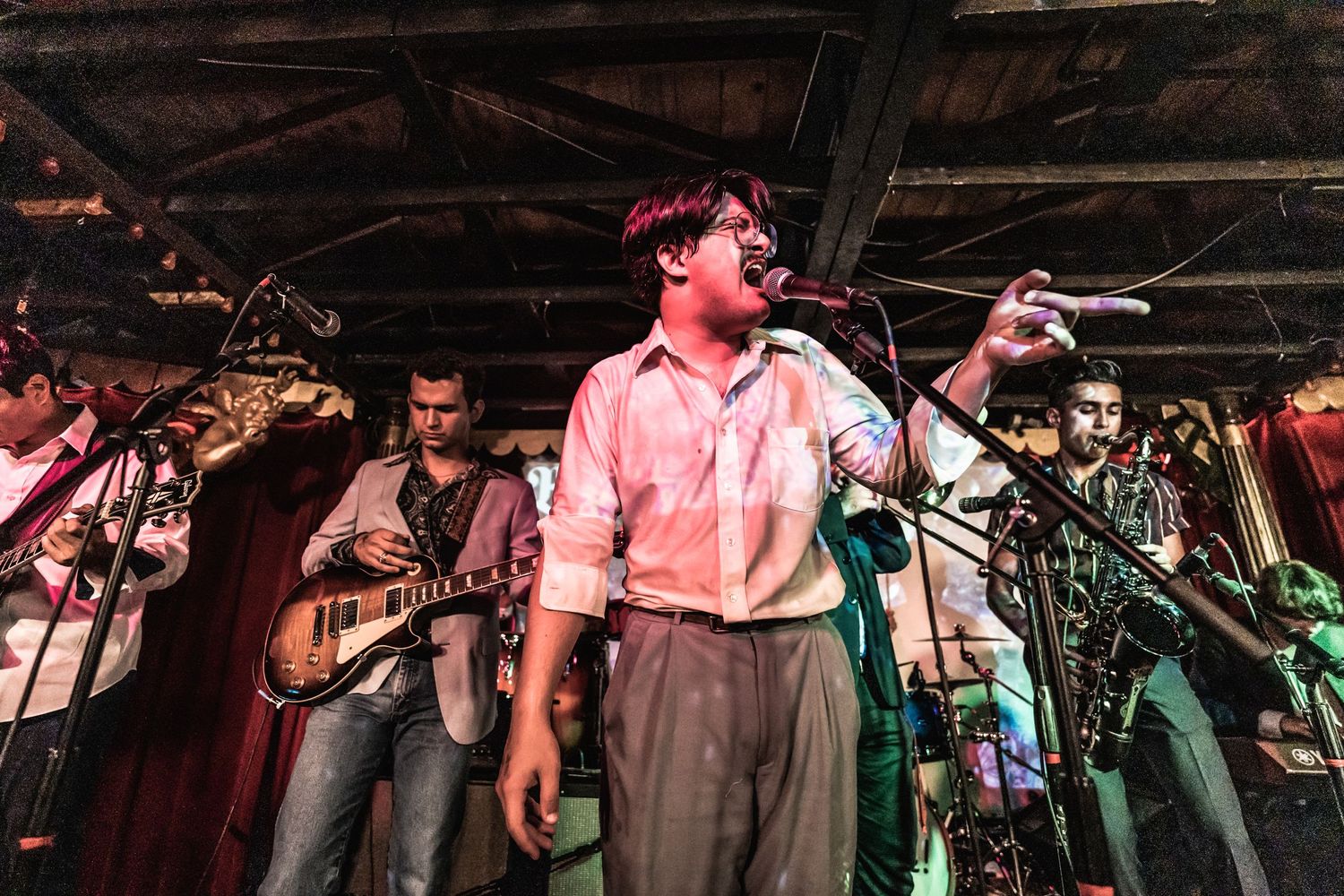 Live band performs on stage with lead singer and musicians in a dimly lit venue.