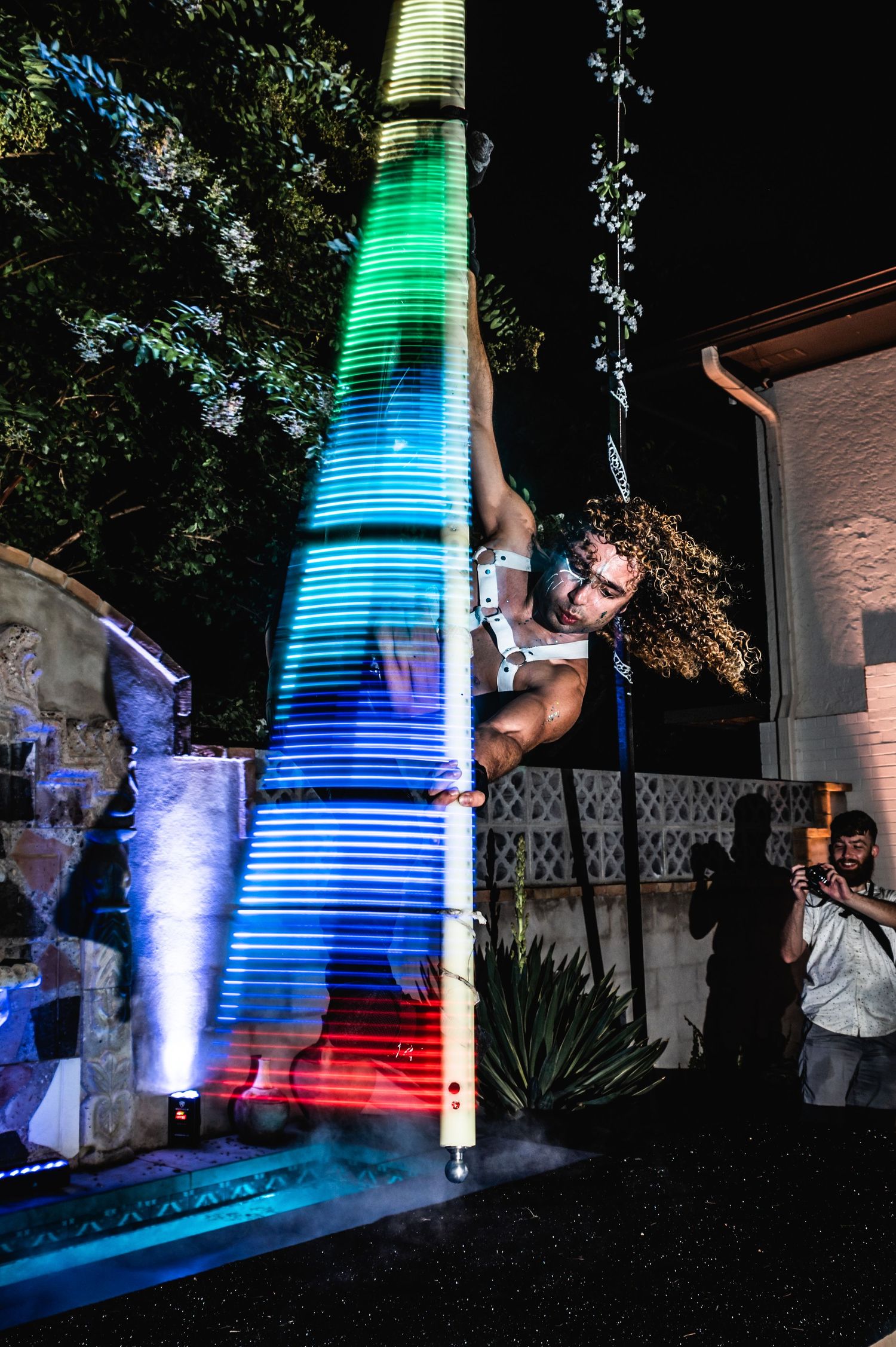 Performer climbing illuminated tower structure with multicolored LED lighting effects.