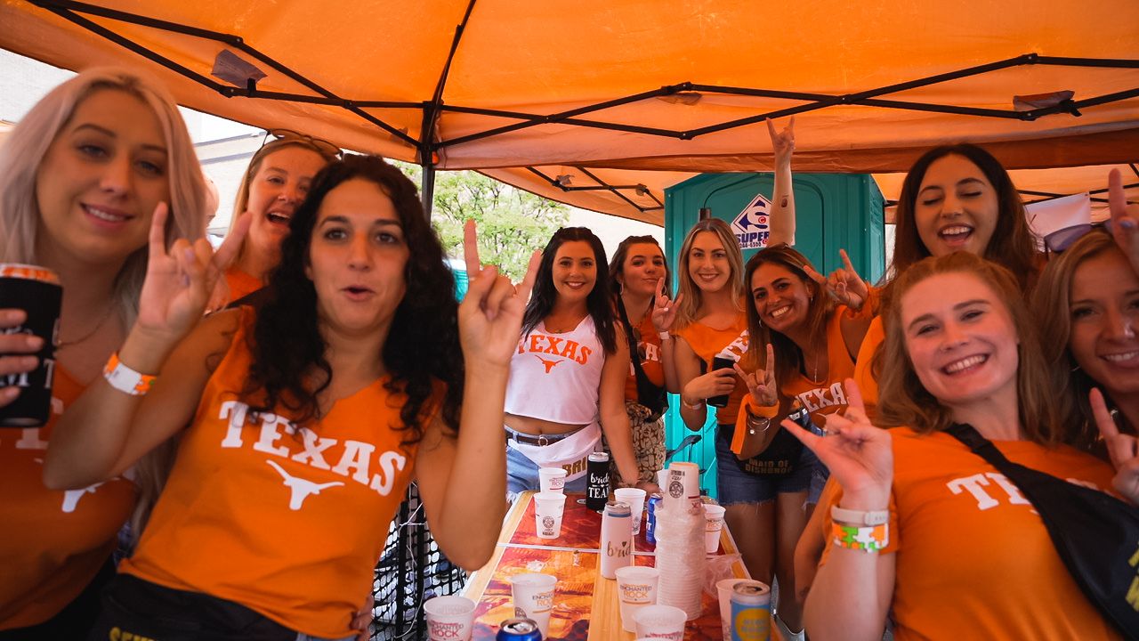 Group wearing orange Texas shirts gathered under tent at outdoor celebration.