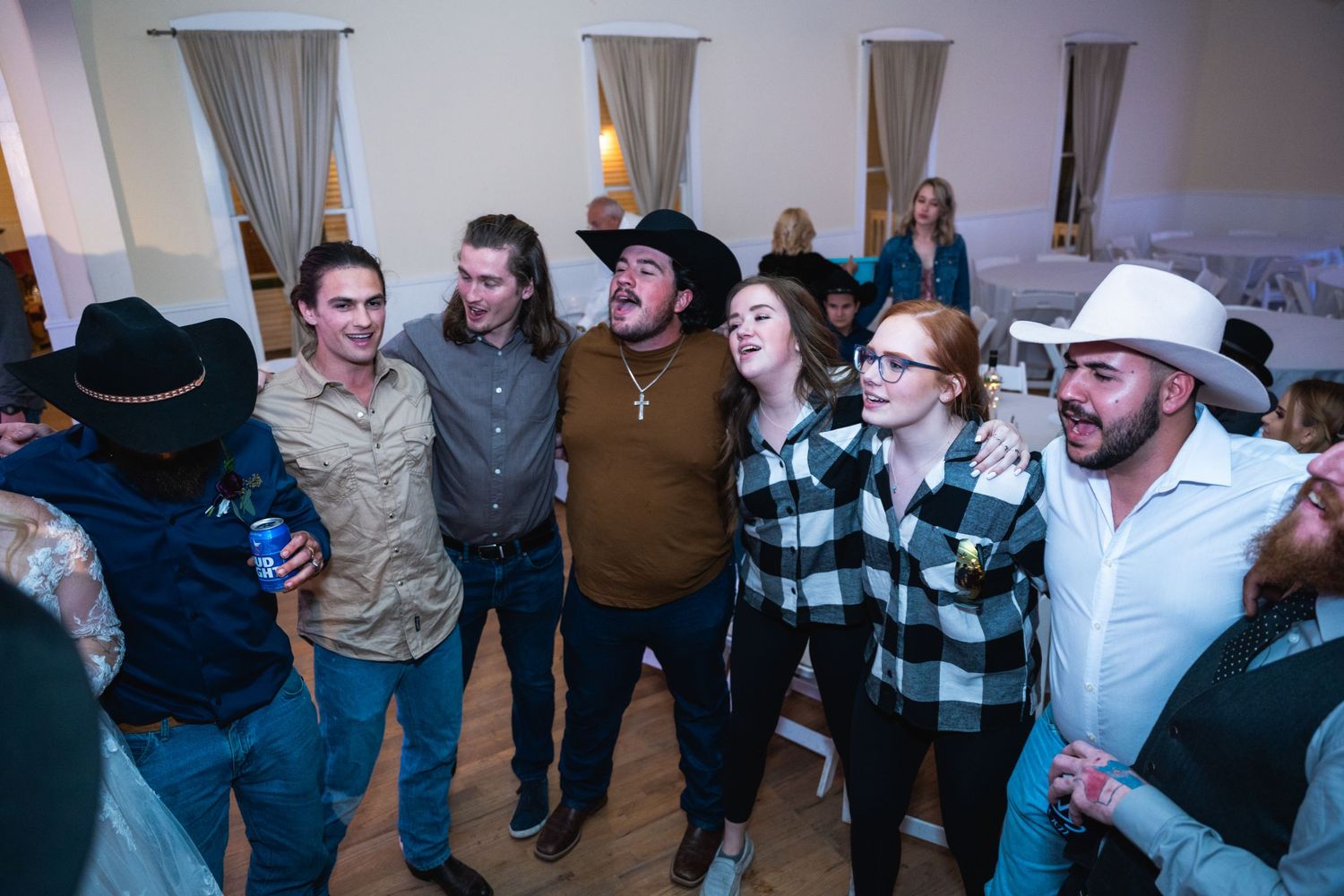 Wedding guests in cowboy hats singing together at a casual indoor celebration.