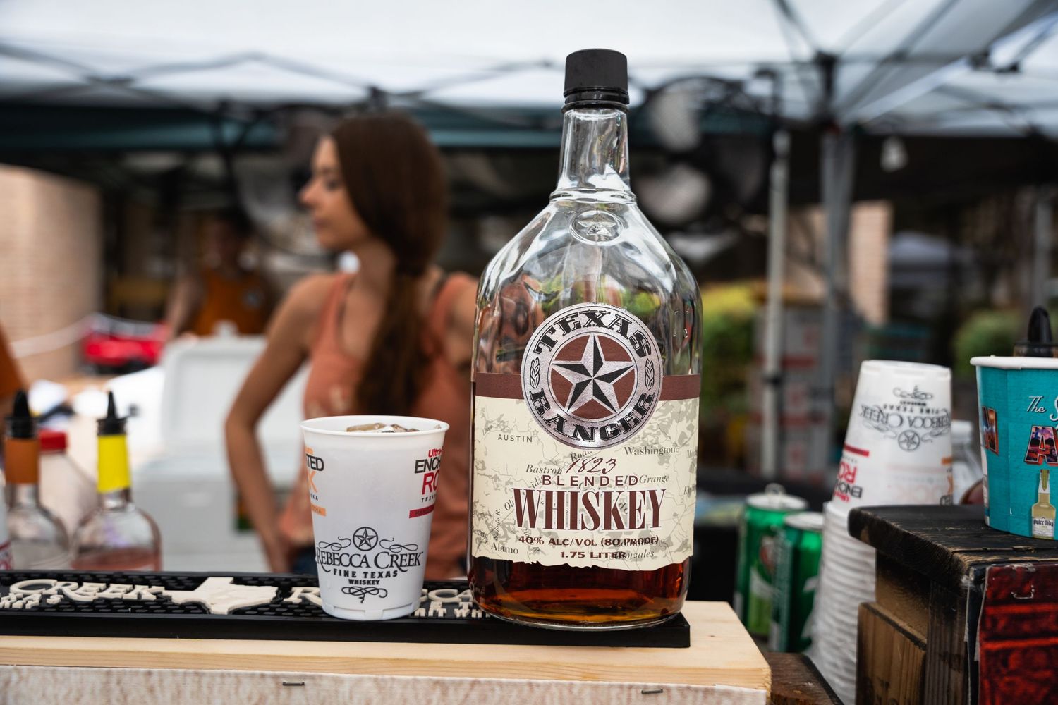A bottle of craft whiskey and shot glass displayed at an outdoor bar event.