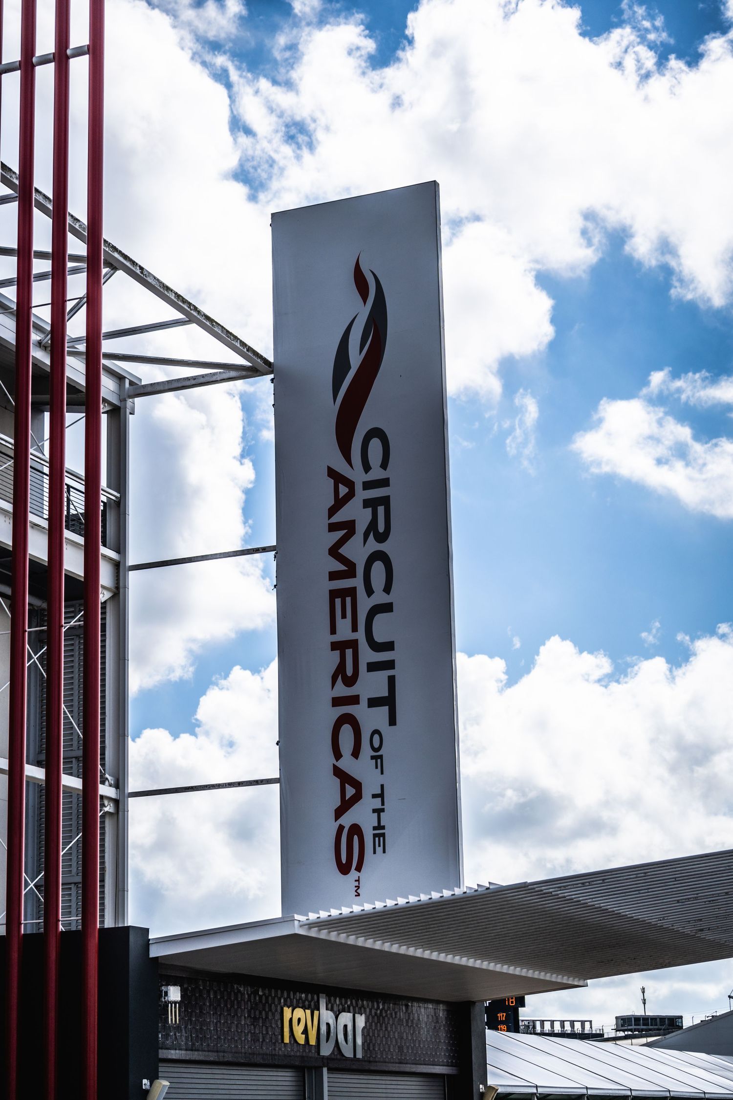 Tall Circuit of the Americas venue signage against blue sky with white clouds.
