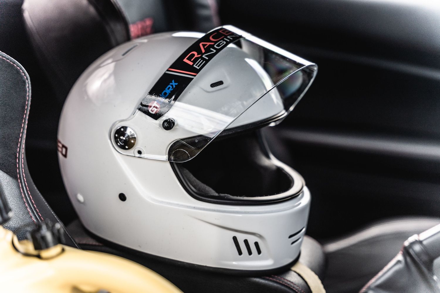A white racing helmet with protective visor sitting inside a vehicle interior.